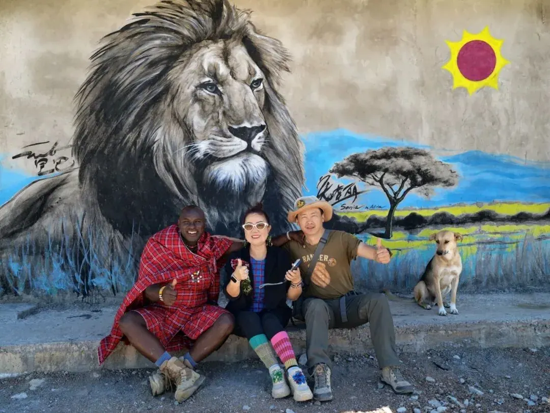 A lion mural at the center, with a Maasai host, a guest and a dog seated in front